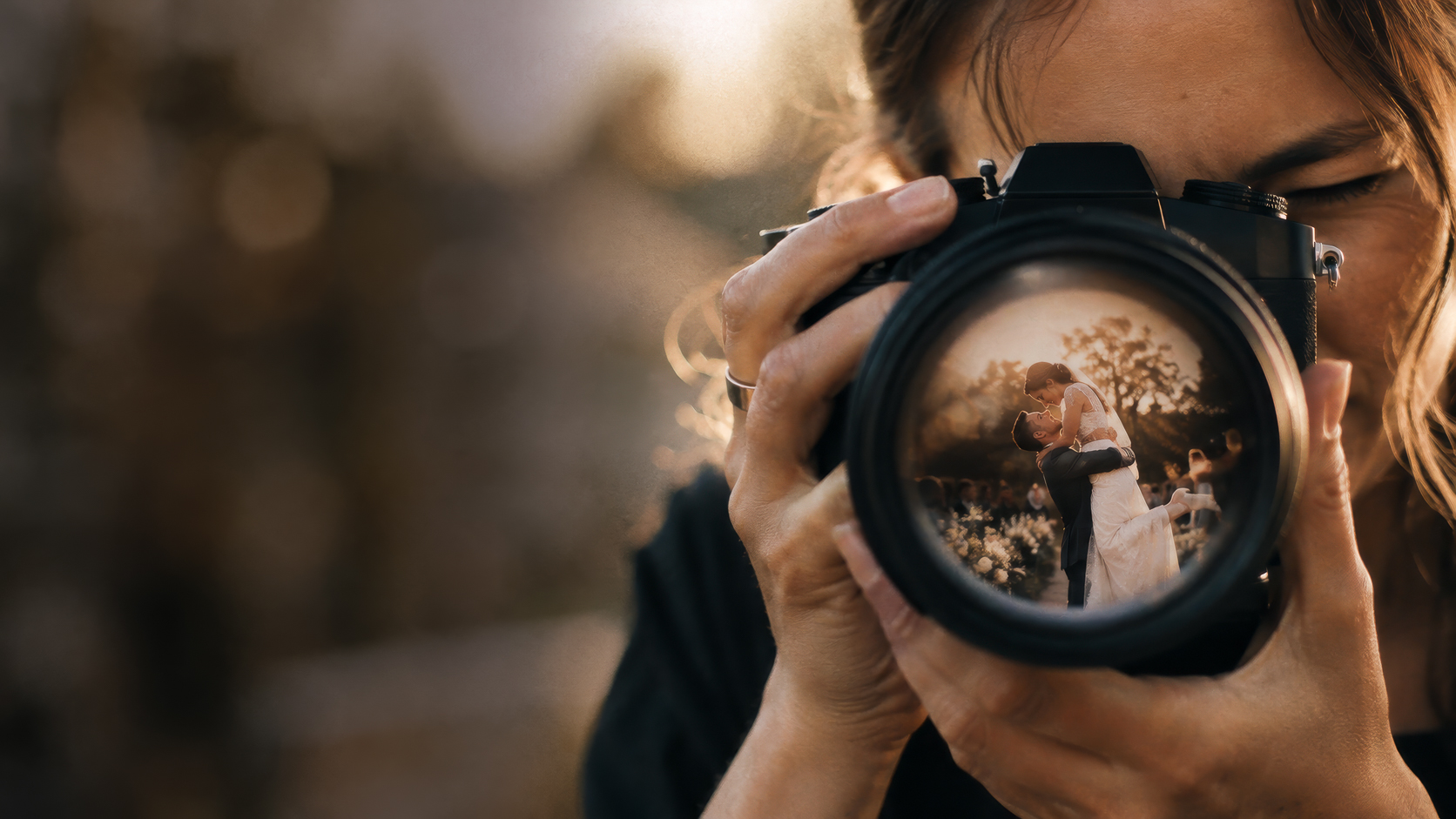 Photographer framing a wedding couple, reflected in the camera lens